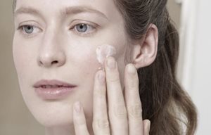 Femme appliquant de la crème sur sa joue gauche.
